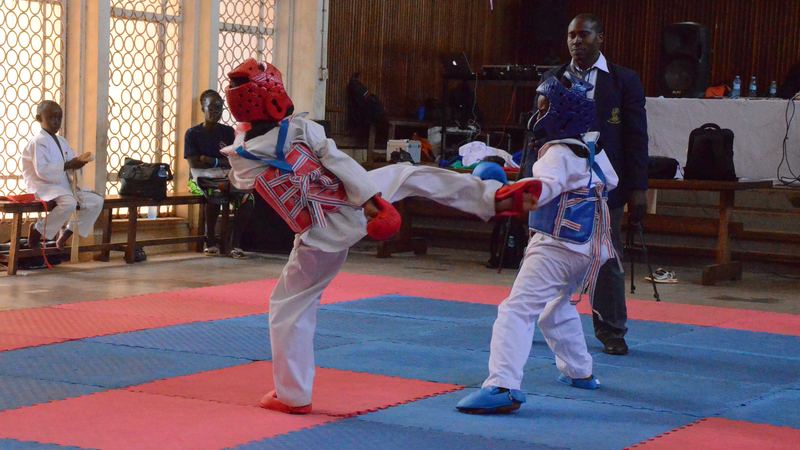 Dua karateka anak dengan pelindung kepala beradu tendangan di atas matras pertandingan